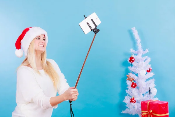 Girl in santa hat taking picture of herself using selfie stick — Stock Photo, Image