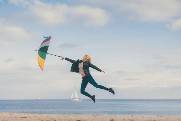 Woman jumping with colorful umbrella on beach — Stock Photo, Image