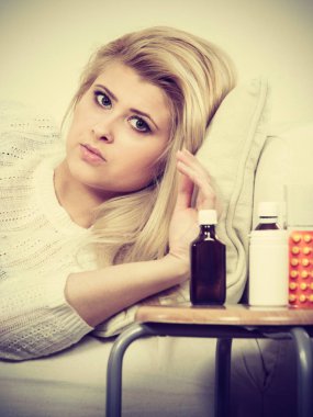 Yatan hasta üzgün bir kadın korkunç gribi sahip kanepe, ilaçlar ve yanında duran haplar ile masa.