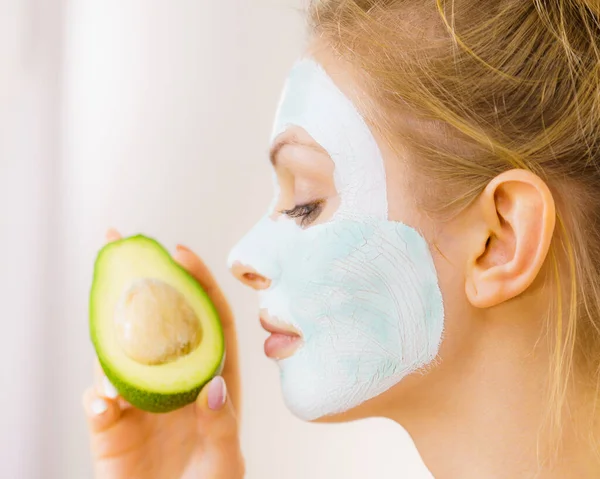 Chica máscara de barro facial sostiene fruta de aguacate —  Fotos de Stock