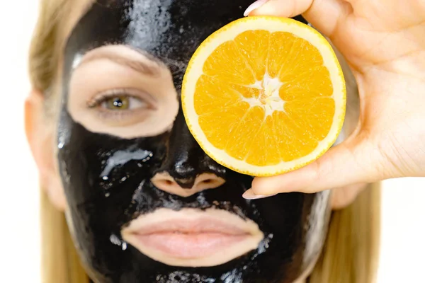 Girl black carbo mask on face holds orange fruit — Stok Foto