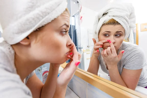 Mujer mirando en el espejo tratando con el acné — Foto de Stock