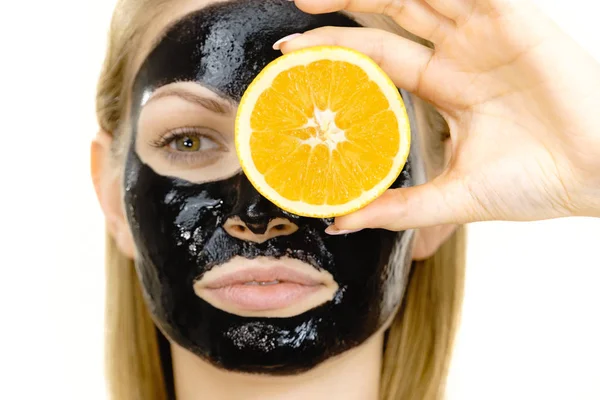 Girl black carbo mask on face holds orange fruit — Stok Foto