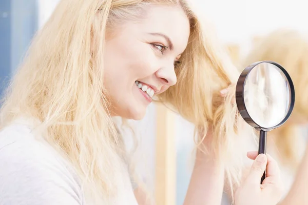 Happy woman looking through magnifer at hair