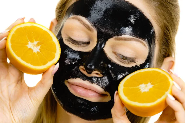 Girl black carbo mask on face holds orange fruit — Stok Foto