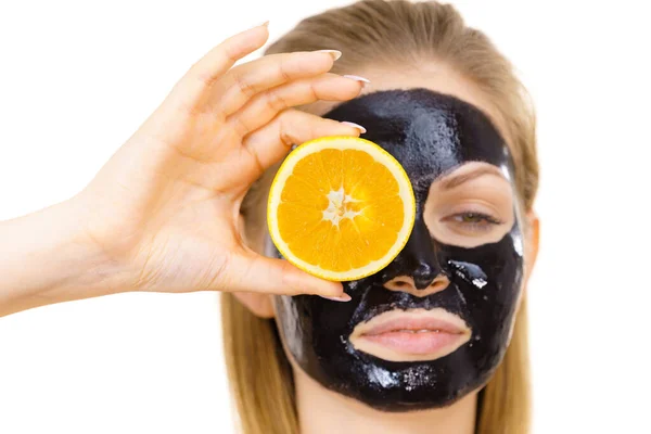 Girl black carbo mask on face holds orange fruit — Stok Foto