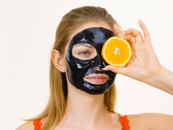 Girl black carbo mask on face holds orange fruit — Stok Foto