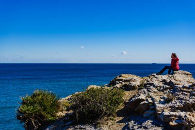 Murcia bölgesindeki İspanyol kayalık kıyı şeridindeki turist kadın. Akdeniz kıyısı manzarası, Calblanque Bölgesel Parkı.