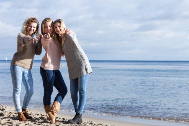 Üç modaya uygun kız kardeş sıcak sonbahar havasında kazak giyip boş zamanlarını güneşli plajlarda geçiriyorlar. Moda modelleri dışarıda.