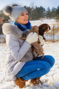 Genç bir kadın dışarıda karda eğleniyor. Dişi, soğuk kış gününde küçük safkan köpekleriyle oynuyor..