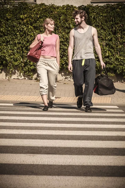 屋外の歩行者横断歩道を渡るスポーツ バッグで幸せなカップルの男女 アクティブな若い女の子とトレーニングの男はスーツ スポーツウェアです — ストック写真