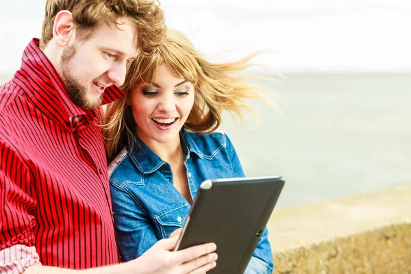 Modern technology devices and tourism concept. Young couple outdoor against sea water with tablet enjoying summer holidays