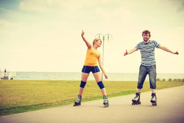 Holidays, active people and friendship concept. Young fit couple on roller skates riding outdoors on sea shore, woman and man rollerblading together on the promenade