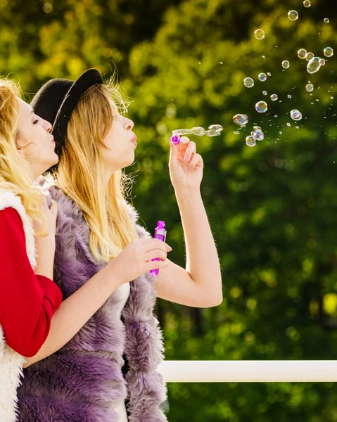 两位年轻时尚女性最好的朋友一边在户外享受阳光灿烂的日子 一边用玩具泡泡棒一起吹泡泡 幸福和无忧无虑的概念 — 图库照片