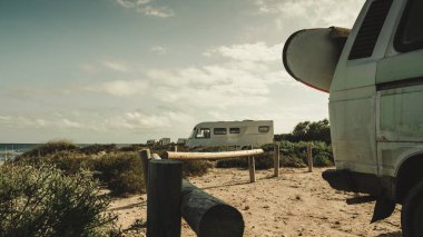 Plaj kıyısında sörf tahtası olan bir karavan. Tatiller, spor ve macera konsepti.