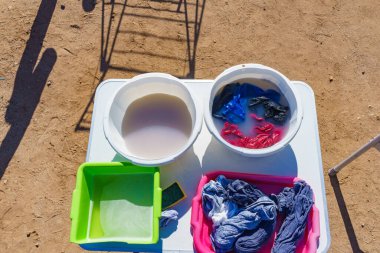 Dışarıda yıkanmadan önce elbiselerini ıslat. Sabunlu su ve çamaşırlı kase. Doğada kamp yapmak..