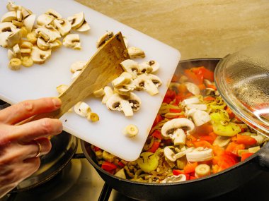 Lezzetli akşam yemeği yemek yapma. El karışık sebze ile sıcak tavaya taze dilimlenmiş mantar ekleyerek.