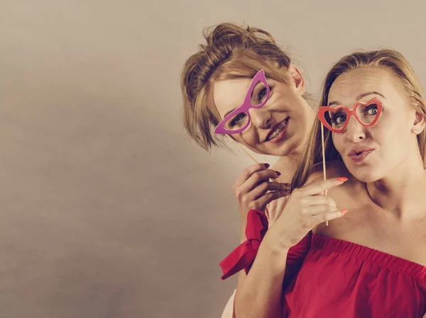 快乐的两个女人拿着纸装饰照片亭面具眼镜在棍子上 玩得很开心 生日和狂欢节有趣的配件概念 — 图库照片