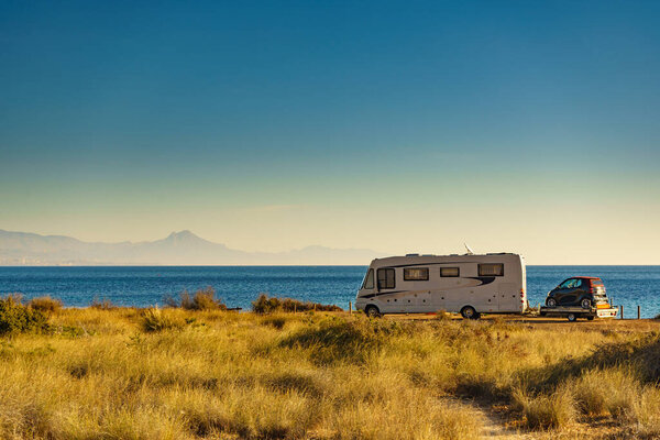 Camper on sea coast with with little car on platform, Spain. Camping on nature beach. Holidays and traveling in motor home.