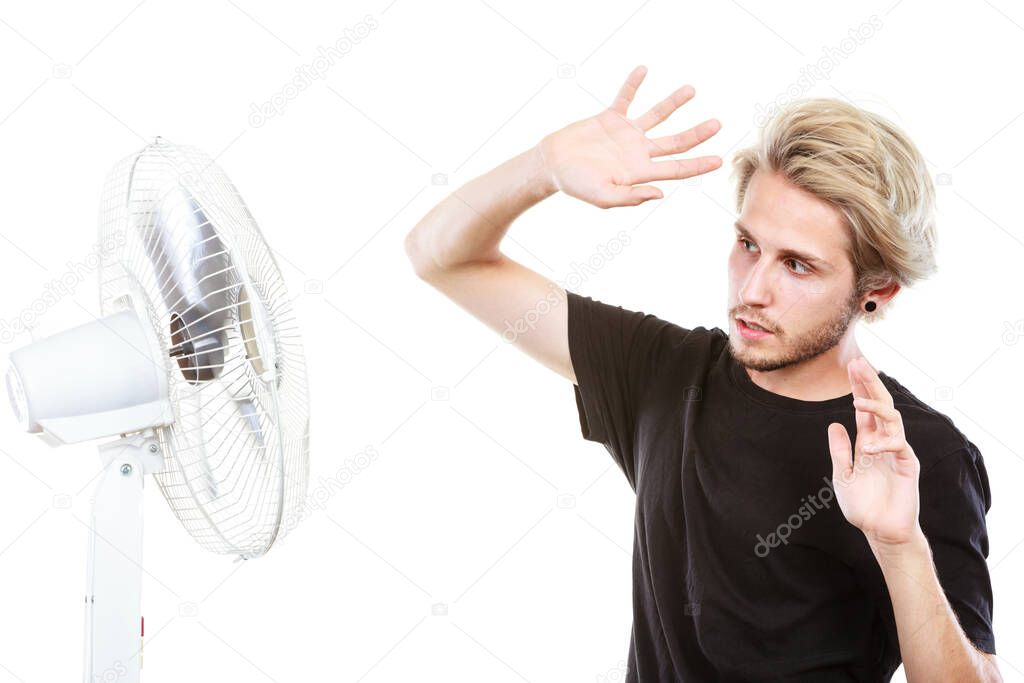 Air conditioning, heat, artistic concept. Young man in front of cooling fan, artistic way fighting with wind holding his hair, studio shot isolated.