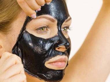 Karbonhidratlı siyah maskesini yüzünden, beyazın üstüne çıkaran genç bir kadın. Genç kız yağlı cildiyle ilgileniyor, gözenekleri temizliyor. Güzellik tedavisi. Cilt bakımı.