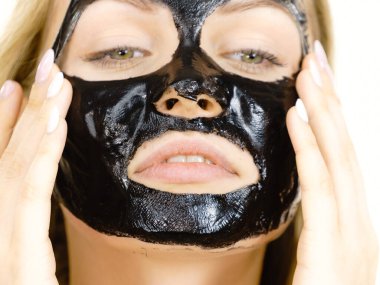 Yüzünde karbonhidratlı siyah kabuk soyma maskesi olan genç bir kadın. Kozmetik, beyazın üzerinde çıkarmaya hazır. Yağlı ciltle ilgilenen genç bir kız. Güzellik tedavisi. Cilt bakımı.