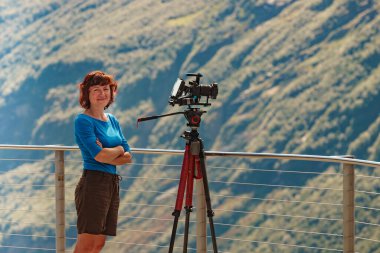 Üç ayaklı kameralı kadın turist seyahat fotoğrafları çekiyor. Norveç, Ornesvingen izleme platformundan dağların tadını çıkarıyor..