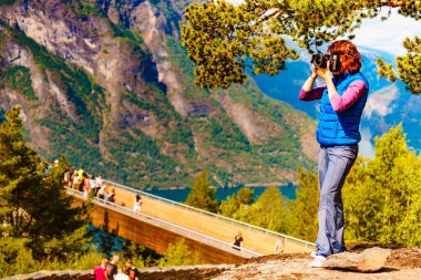 Stegastein gözcü üzerinde Turist kadın kamera seyahat resmi ile alarak, fiyort dağları manzara zevk. Norveç'te Ulusal turistik manzaralı rota Aurlandsfjellet