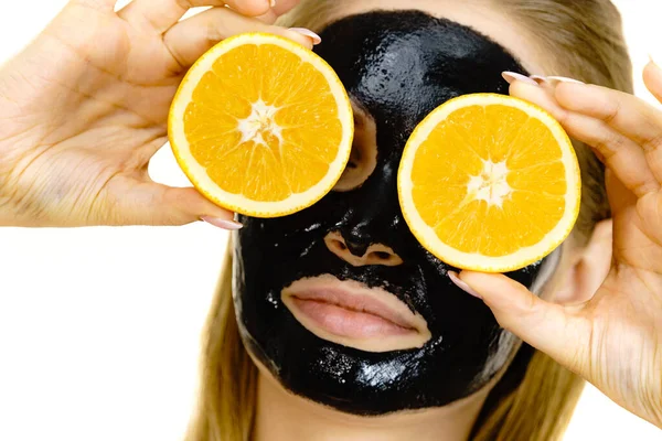 顔にカルボデトックスブラックピールオフマスクを持つ女性は オレンジフルーツを保持しています 十代の女の子は油性の肌の世話をし 毛穴をきれいにします 美の治療だ スキンケア — ストック写真