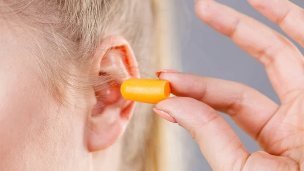 Woman putting ear plugs into her ears getting rid on noise in loud place.