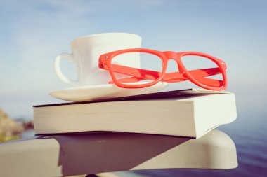 Tatillerde kitap okumak. Kahve fincanı ve kitap açık havada mavi deniz suyuna karşı sandalyede..