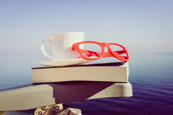 休日の読書 コーヒーカップと青い海の背景に対する屋外の椅子の上の本 — ストック写真