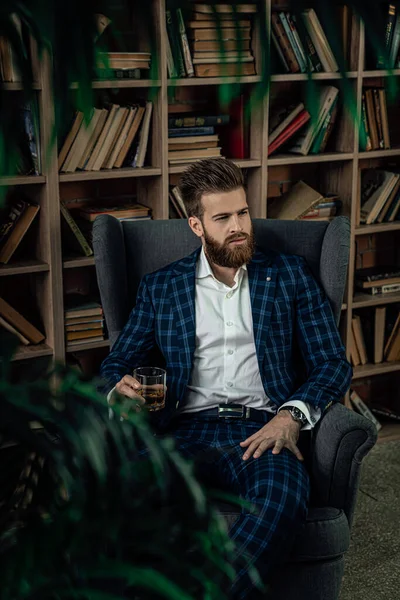 Elegante hombre en un traje con vaso de bebida sentado en habitación vintage y libro de lectura. Hombre de moda . —  Fotos de Stock