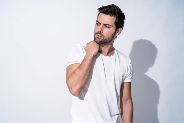 Portrait of handsome young man in casual wear looking away and smiling while standing against grey background