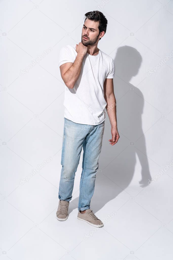 Full length of handsome young man in casual wear looking away and smiling while standing against grey background
