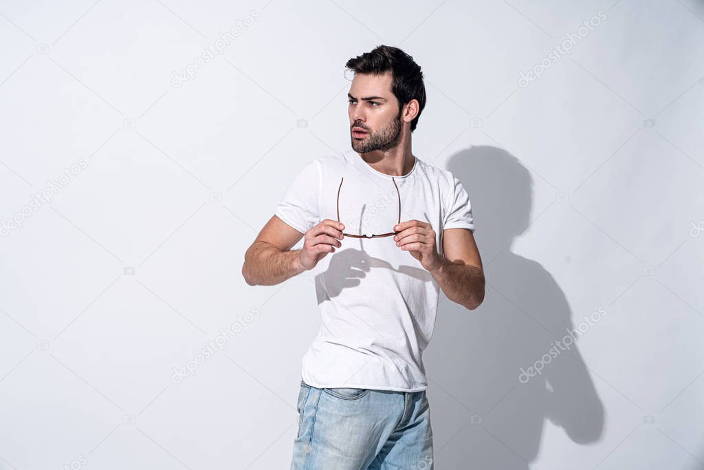 Full length of handsome young man in eyewear and casual wear looking away while standing against grey background