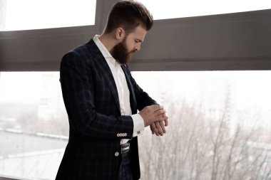 Gitme vakti geldi. Mavi takım elbiseli yakışıklı bir adam evde bir kafesin içinde pencerenin yanında duruyor ve saati kontrol ediyor..