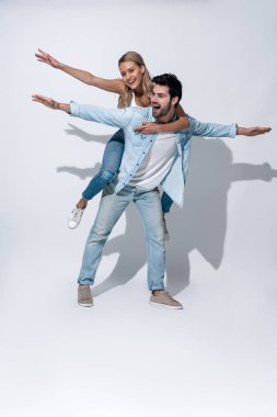 Neşeli hissediyorum. Tam boy yakışıklı genç adam gri arka planda dururken kız arkadaşını sırtında taşıyor..
