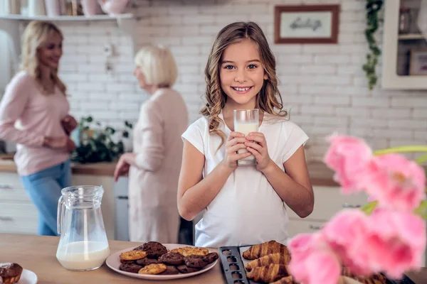 Schöne Mädchen mit einem Glas Milch blickt in die Kamera. Tochter, Mutter und Großmutter kochen in der Küche. Frauengeneration backt gemeinsam. — Stockfoto