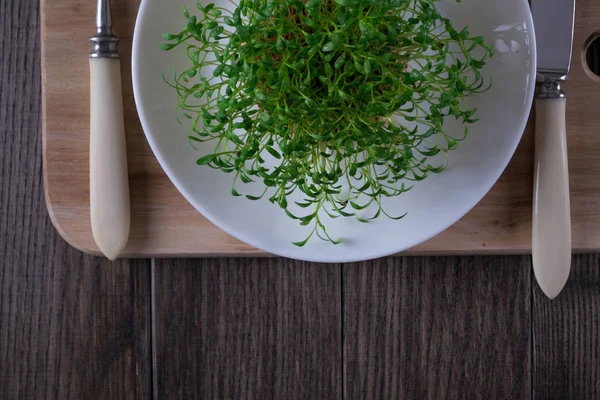 Portion of fresh Garden Cress  on wooden background with fork and knife
