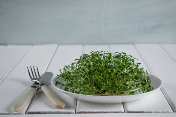 Garden cress on white plate with fork and knife