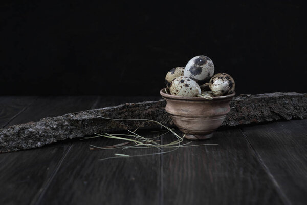 Quail eggs in clay pot on dark background. Eco products.