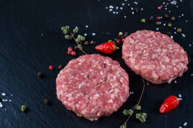 Taze çiğ et burger pirzola otlar ve baharatlar için arka plan siyah arduvaz gemide.