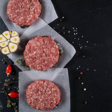 Taze çiğ et burger pirzola otlar ve baharatlar için arka plan siyah arduvaz gemide. 