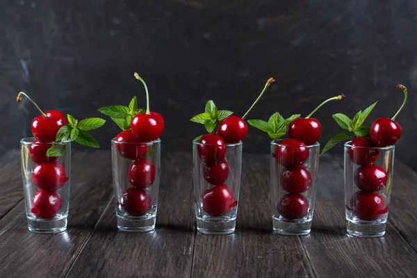 Una fila de pilas de vidrio con cerezas y hojas de menta —  Fotos de Stock