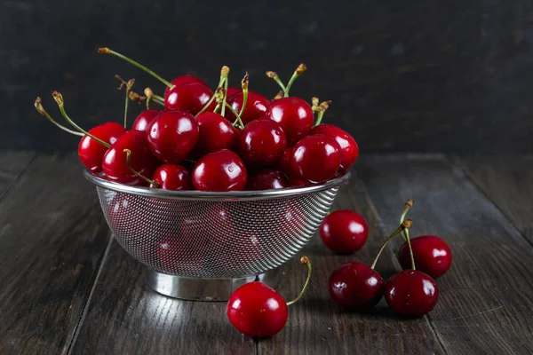 Fresh cherry in a metal sieve herbs on dark wooden background. — Stock Photo, Image
