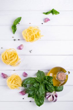 Sarımsak, zeytinyağı ve pişmemiş makarna beyaz masa üzerine taze yeşil fesleğen. Düz yatıyordu.