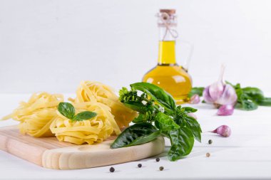 Sarımsak, zeytinyağı ve pişmemiş makarna beyaz masa üzerine taze yeşil fesleğen