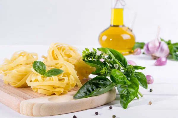 Sarımsak, zeytinyağı ve pişmemiş makarna beyaz masa üzerine taze yeşil fesleğen