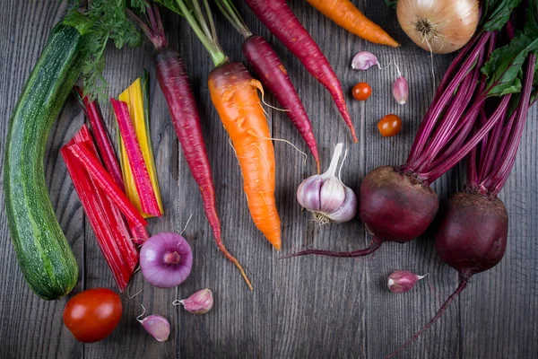 Κάτοψη των φρέσκων λαχανικών, μπαχαρικά σε ρουστίκ σκούρο φόντο. Καρότο, τεύτλα, chard, κολοκυθάκια, κρεμμύδι, σκόρδο, ντομάτα. Έννοια συγκομιδή/κηπουρική. — Φωτογραφία Αρχείου